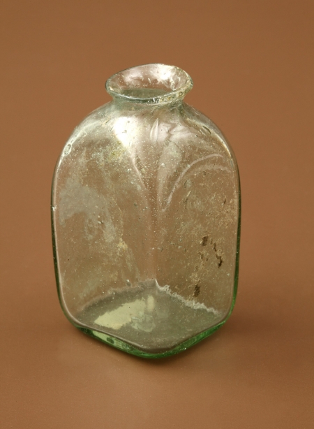 Buteleczka szklana. Należy do typu buteleczek wielobocznych z jednym bokiem wydłużonym, z krótką szyjką i wychylonym wylewem. Została wykonana z zielonego szkła zawierającego pęcherzyki gazowe. Służyła najprawdopodobniej do przechowywania lekarstw lub pachnideł. Znaleziona w zamkowej latrynie użytkowanej od XVI do XVIII wieku.